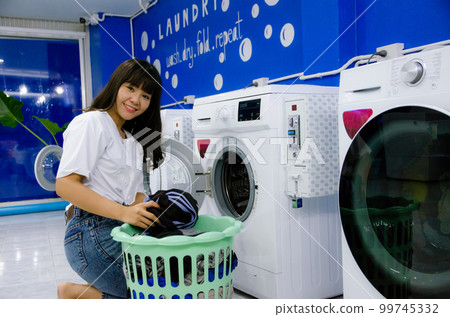 Asian girl is washing cloths by washing machine in laundry shop with smile face Asian girl is washing cloths by washing machine in laundry shop with smile face 99745332
