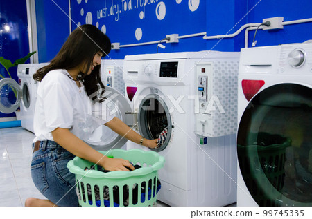 Asian girl is washing cloths by washing machine in laundry shop Asian girl is washing cloths by washing machine in laundry shop 99745335