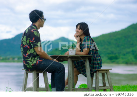 Asian couple are sitting on chair with table on mountain and river background with smile face Asian couple are sitting on chair with table on mountain and river background with smile face 99745336