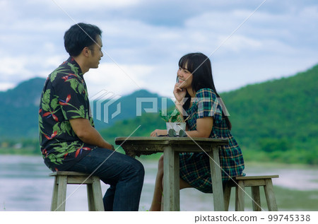 Asian couple are sitting on chair with table on mountain and river background with smile face 99745338