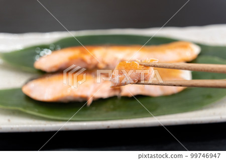 He is picking up grilled salmon from Hokkaido with chopsticks. 99746947