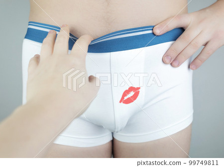 Close-up of a man in white underwear. The girl sticks to the man and stretches her hands to his shorts. Lipstick marks on underpants. A hint of intimacy and oral sex..Photo without a face Close-up of a man in white underwear. The girl sticks to the man and stretches her hands to his shorts. Lipstick marks on underpants. A hint of intimacy and oral sex..Photo without a face 99749811