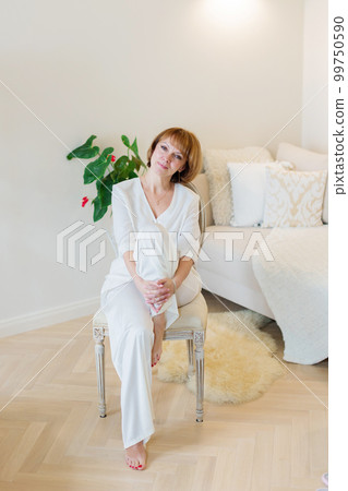 Smiling stylish mature middle aged woman sitting on chair at home in living room and resting. Smiling stylish mature middle aged woman sitting on chair at home in living room and resting. 99750590