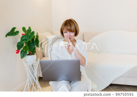 Adult confident pretty woman working with laptop and credit card at home in stylish living room. Adult confident pretty woman working with laptop and credit card at home in stylish living room. 99750591