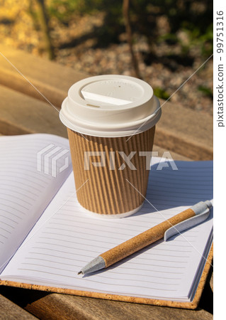 Eco recycling paper cup with coffee or tea on kraft paper with empty paper notebook on wooden bench. Concept of study work outdoors. Take away coffee to go. Copy space for text. Disposable Cardboard Eco recycling paper cup with coffee or tea on kraft paper with empty paper notebook on wooden bench. Concept of study work outdoors. Take away coffee to go. Copy space for text. Disposable Cardboard 99751316