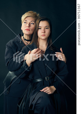 Generations. Beautiful middle-aged woman, mother posing with young girl over dark studio background. Concept of motherhood and family 99751567