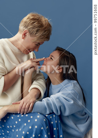 Portrait of happy smiling middle-aged woman and her young daughter posing over blue studio background. Concept of motherhood and family 99751608