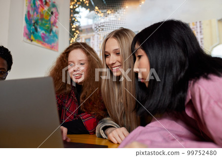 A bunch of young people, girls and guys, work on laptops remotely in a cafe, talk, have fun, take selfies, chat on phones. A bunch of young people, girls and guys, work on laptops remotely in a cafe, talk, have fun, take selfies, chat on phones. 99752480