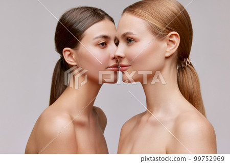Couple of beautiful elegant young women, blond and brunette with well-kept skin posing over light background. Concept of natural beauty, fashion, skin care and health Couple of beautiful elegant young women, blond and brunette with well-kept skin posing over light background. Concept of natural beauty, fashion, skin care and health 99752969