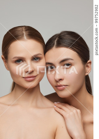 Closeup portrait of two adorable young girls with well-kept skin posing over grey background. Models with bare shoulders. Concept of beauty, spa, skin care and health 99752982