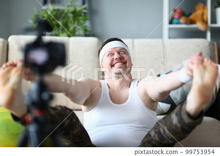 Sports male blogger doing morning exercises warming up in living room in front of camera Sports male blogger doing morning exercises warming up in living room in front of camera 99753954