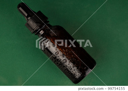 Cosmetic bottle with water droplets on green background. Top view with space for copy. 99754155