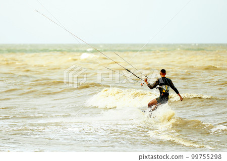 A young kiteboarder rides the waves into the sea A young kiteboarder rides the waves into the sea 99755298