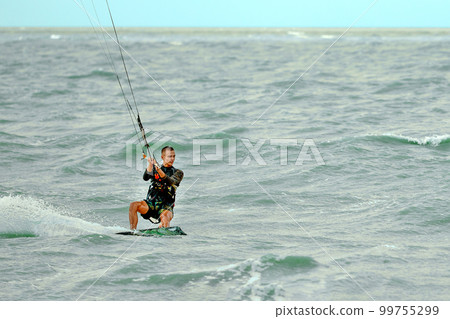 A young kiteboarder rides the waves into the sea A young kiteboarder rides the waves into the sea 99755299