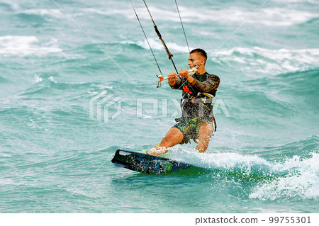 A young kiteboarder rides the waves into the sea A young kiteboarder rides the waves into the sea 99755301