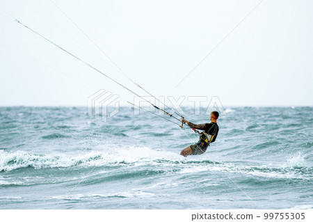 A young kiteboarder rides the waves into the sea A young kiteboarder rides the waves into the sea 99755305