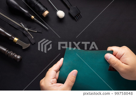 Leather Craftsman holding green leather sample and tool kit for handcraft wallets. 99758048