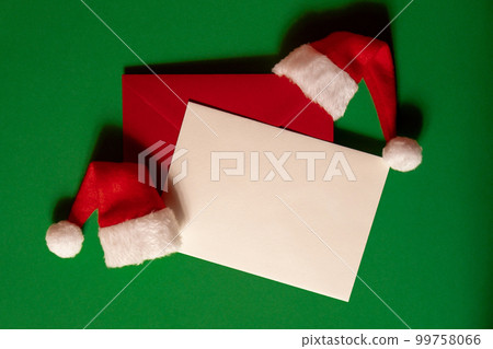Santa hat with empty paper card note envelope on green background. Copy space for your text. Mock up for advertisement. Holiday Christmas composition Santa hat with empty paper card note envelope on green background. Copy space for your text. Mock up for advertisement. Holiday Christmas composition 99758066