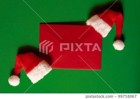 Santa hat with empty paper card note envelope on green background. Copy space for your text. Mock up for advertisement. Holiday Christmas composition Santa hat with empty paper card note envelope on green background. Copy space for your text. Mock up for advertisement. Holiday Christmas composition 99758067