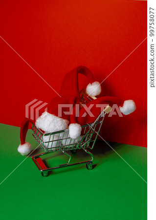 Santa hat in shopping trolley on isometric red green background. Online shopping holiday concept Copy space for your text. Mock up for advertisement. Holiday Christmas composition. Minimalistic Santa hat in shopping trolley on isometric red green background. Online shopping holiday concept Copy space for your text. Mock up for advertisement. Holiday Christmas composition. Minimalistic 99758077