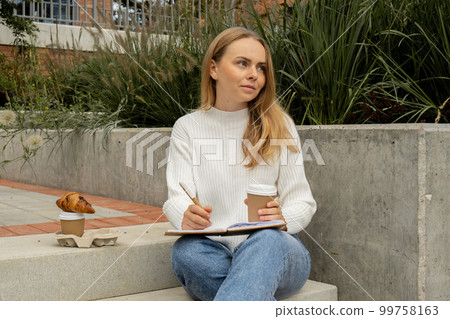Young student study with notebook in park. Drinking coffee and eat croissants. Writing gratitude journal self reflection self discovery 99758163