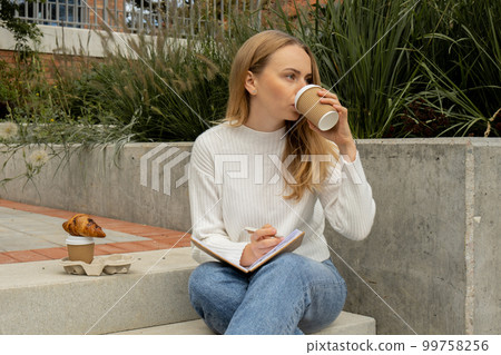 Young student study with notebook in park. Drinking coffee and eat croissants. Writing gratitude journal self reflection self discovery Young student study with notebook in park. Drinking coffee and eat croissants. Writing gratitude journal self reflection self discovery 99758256