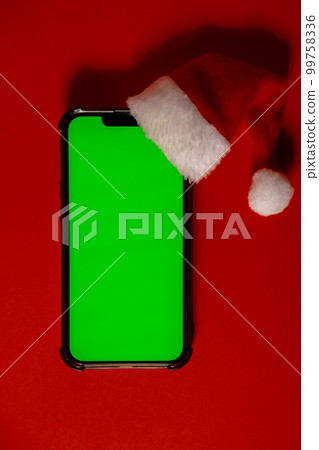 Mobile phone dressed in Santa-Claus red-white hat with chroma key screen against red background. Concept for Christmas or New Years holidays. Blank cell phone. Digital gadget wireless wishlist concept Mobile phone dressed in Santa-Claus red-white hat with chroma key screen against red background. Concept for Christmas or New Years holidays. Blank cell phone. Digital gadget wireless wishlist concept 99758336