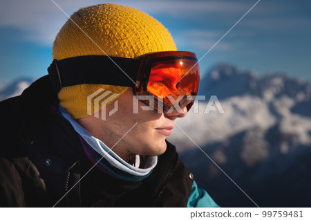 Male skier overlooking snow covered mountains on a sunny day, sun beams reflection in ski goggles Male skier overlooking snow covered mountains on a sunny day, sun beams reflection in ski goggles 99759481
