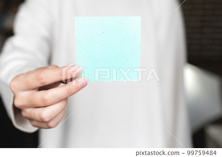 woman is holding a note with blank space. A woman is holding a square empty blank sticker in her hands. Close up background space for text woman is holding a note with blank space. A woman is holding a square empty blank sticker in her hands. Close up background space for text 99759484