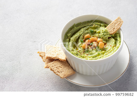 avocado hummus in white bowl with chickpeas, parsley, spices and rice crackers 99759682