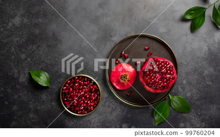 ripe red pomegranate and green leaves on a dark concrete background. 99760204