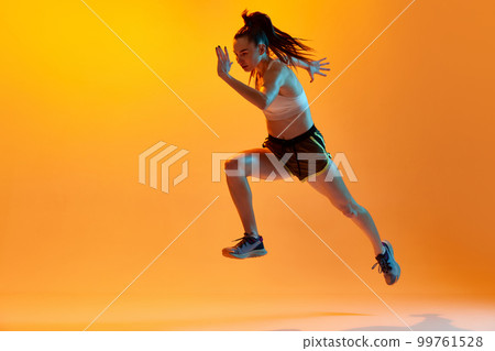 Running. Dynamic image of professional female runner, athlete training over orange studio background in neon light. Concept of sport. health and strength Running. Dynamic image of professional female runner, athlete training over orange studio background in neon light. Concept of sport. health and strength 99761528