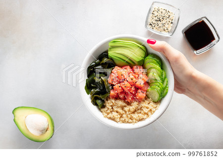female hand holding poke bowl with quinoa, salmon, avocado, cucumber, wakame seaweed. female hand holding poke bowl with quinoa, salmon, avocado, cucumber, wakame seaweed. 99761852