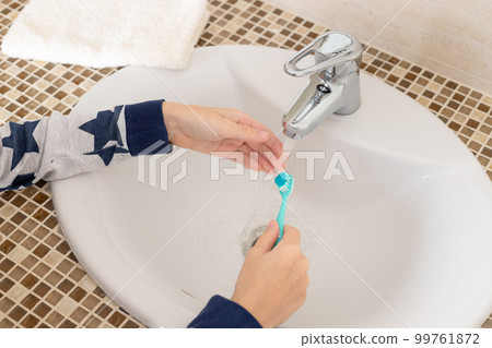 Children's hands holding toothbrush over sink in bathroom 99761872
