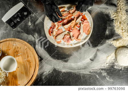Cooking pizza on a steel table; dough, flour, pizza topping, sauce and chef`s hands in black gloves on the table 99763098