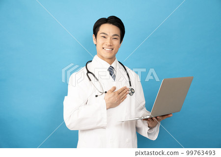Male doctor smiling with a laptop on blue background 99763493