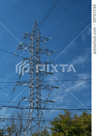 Tower with high-voltage energy transmission wires against the blue sky. High-voltage tower. Electrical wires and fuses. Energy business. Energy industry. Import and export of energy. Tower with high-voltage energy transmission wires against the blue sky. High-voltage tower. Electrical wires and fuses. Energy business. Energy industry. Import and export of energy. 99763598