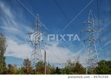 Tower with high-voltage energy transmission wires against the blue sky. High-voltage tower. Electrical wires and fuses. Energy business. Energy industry. Import and export of energy. 99763599