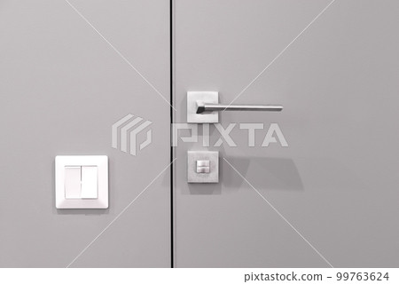 Closed hidden, gray interior door with a handle and a switch on the wall. Closed hidden, gray interior door with a handle and a switch on the wall. 99763624