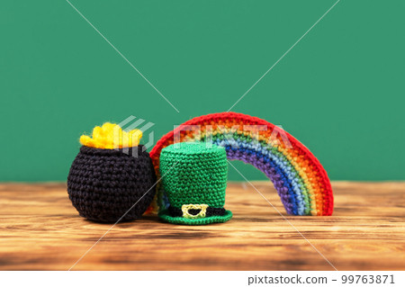 St Patrick's Day concept. Composition of a green hat, knitted black cauldron with coins and a seven-colored bright rainbow on a wooden background. Postcard for the holiday, copy space 99763871