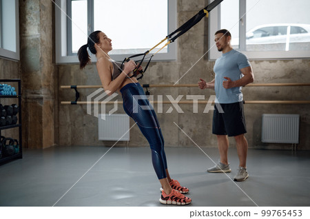 Woman training with suspension straps under professional sport coach control 99765453