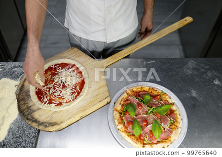 Above view on chef hand preparing pizza base on professional kitchen Above view on chef hand preparing pizza base on professional kitchen 99765640