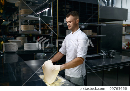 Chef tossing dough in air while making pizza base 99765666