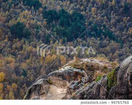 Minimalistic landscape of a rocky ledge against the background of a mountain forest. The edge of a stone cliff, a dangerous gorge. Minimalistic landscape of a rocky ledge against the background of a mountain forest. The edge of a stone cliff, a dangerous gorge. 99765768