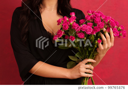A woman in a black dressing gown with a deep neckline holds a bouquet of pink roses, on a pink background, close-up 99765876