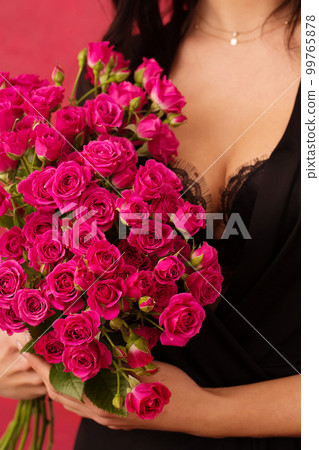 A woman in a black dressing gown with a deep neckline holds a bouquet of pink roses, close-up 99765878