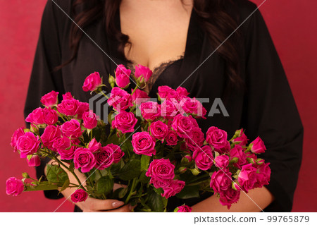 A woman in a black sexual dressing gown with a deep neckline holds a bouquet of pink roses, close-up 99765879