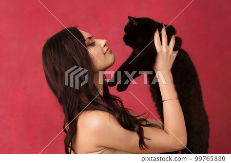 A beautiful dark-haired woman plays with a black cat, profile photo on a pink background 99765880