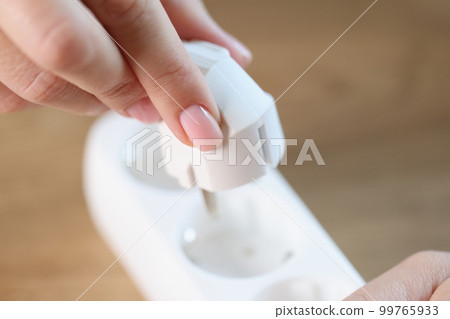 Female hand inserting electric plug into white socket 99765933