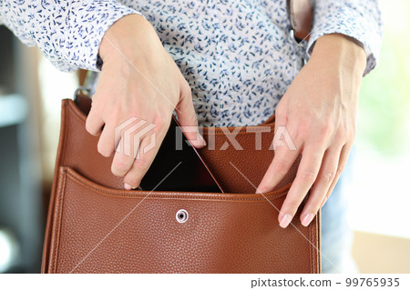 Woman putting smartphone in brown leather crossbody Woman putting smartphone in brown leather crossbody 99765935